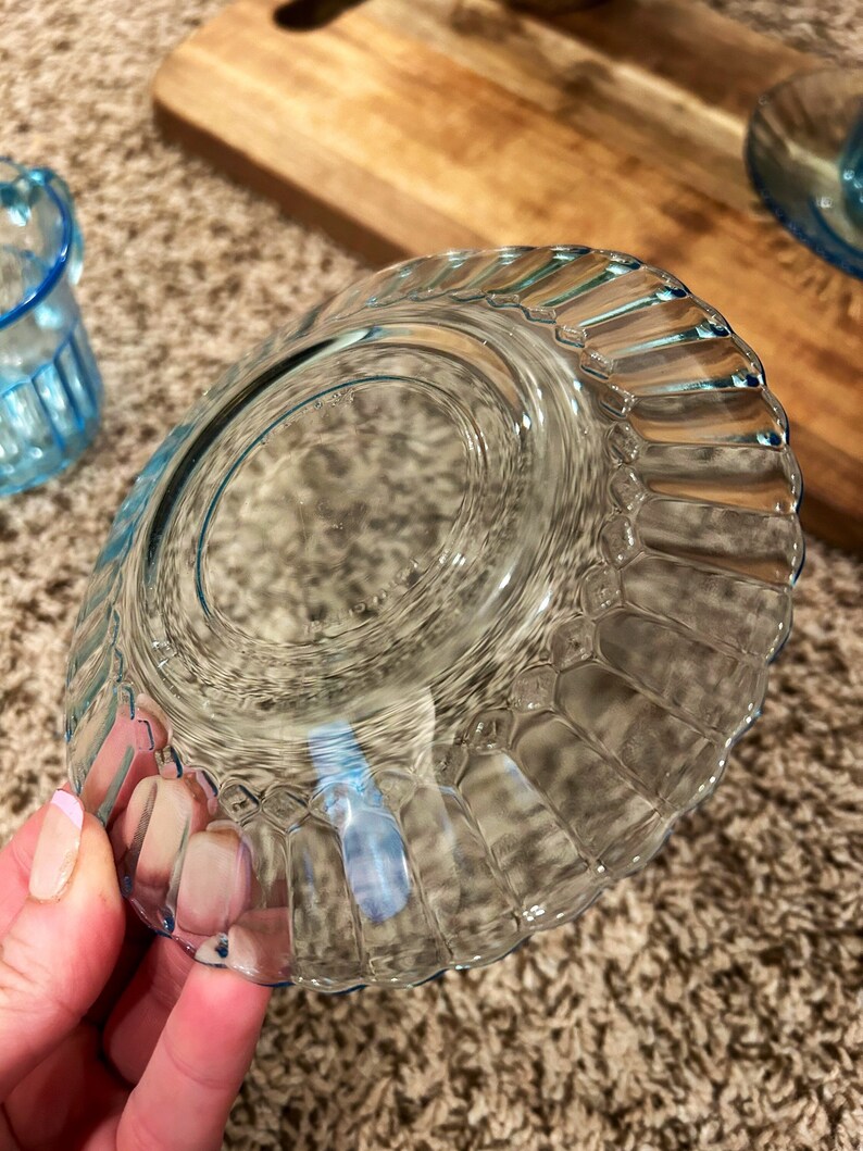 May include: A clear blue glass saucer with a fluted edge. The saucer is empty and has a slight blue tint.