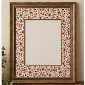 May include: A rectangular picture frame with a metallic bronze finish and a beaded inner edge. The frame features a wide matting border decorated with a repeating pattern of small red flowers and green leaves on an off-white background.