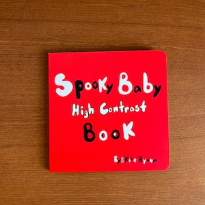 May include: A red square book titled "Spooky Baby High Contrast Book" with white and black text. The book's cover features the title in a playful font, designed for babies. The author's name, "Kate Bynum," is at the bottom.