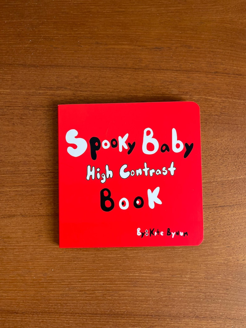 May include: A red square book titled "Spooky Baby High Contrast Book" with white and black text. The book's cover features the title in a playful font, designed for babies. The author's name, "Kate Bynum," is at the bottom.