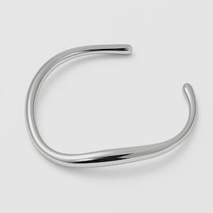 May include: A polished silver-tone cuff bracelet with a smooth, rounded, and slightly irregular organic shape. The open-ended design features a continuous, flowing metal band that tapers slightly towards the rounded ends, creating a sleek look.