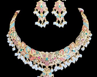 Op de afbeelding: Een gouden ketting en oorbellen set met een bloemmotief en gekleurde edelstenen. De ketting heeft een hanger met een parel druppel en de oorbellen hebben parel druppels.