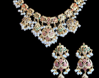 Op de afbeelding: Een gouden ketting en oorbellenset met ingewikkelde bloemmotieven, bezet met gekleurde stenen en parels. De ketting heeft een hanger in druppelvorm en de oorbellen zijn van het hangende type.