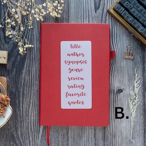 Pode incluir: Um di&aacute;rio de capa dura vermelho com um r&oacute;tulo branco na frente. O r&oacute;tulo tem as palavras "t&iacute;tulo", "autor", "sinopse", "g&ecirc;nero", "revis&atilde;o", "classifica&ccedil;&atilde;o", "favorito" e "cita&ccedil;&otilde;es" escritas nele. O di&aacute;rio est&aacute; sobre uma superf&iacute;cie de madeira.