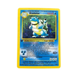May include: A Blastoise Pokémon trading card with a blue and yellow design. The card features a blue Blastoise character with a shell and text that reads "Blastoise" and "100 HP". The card also includes text describing the character's abilities and stats.