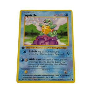 May include: A 1999 Squirtle trading card with a yellow border and blue background. The card features an illustration of a green turtle-like creature on purple rocks, with text including 40 HP, Bubble, Withdraw, and physical stats of 1' 8" and 20 lbs.