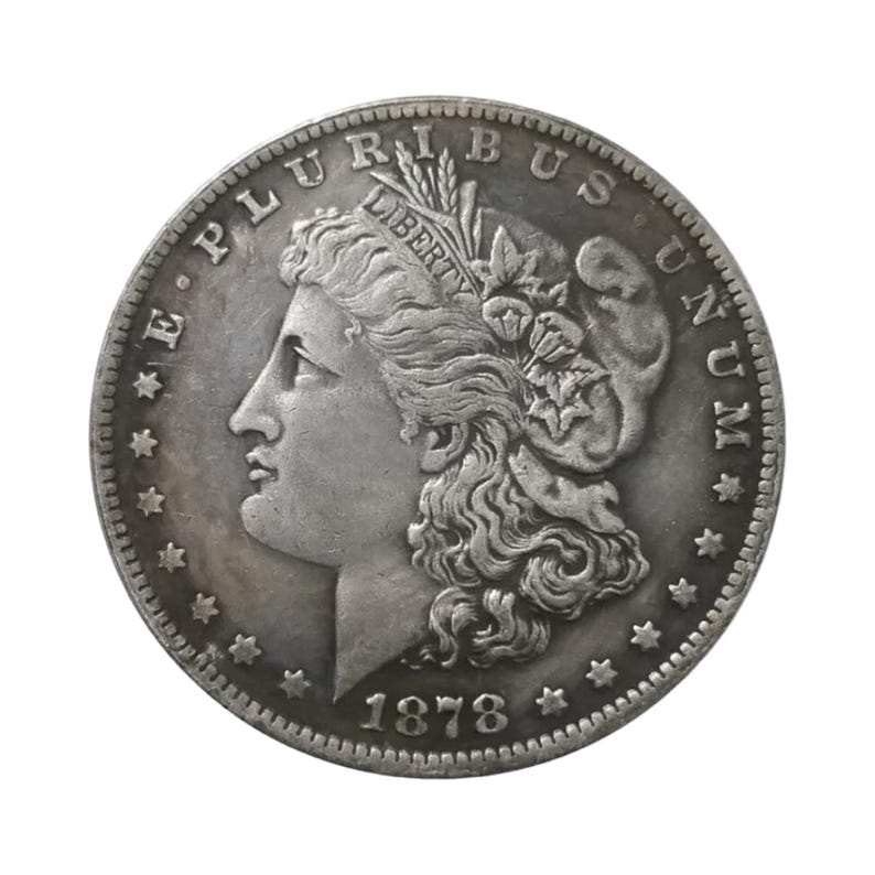 Pu&ograve; includere: Una moneta da un dollaro Morgan color argento del 1878 raffigurante il profilo di Lady Liberty rivolto a sinistra, che indossa un berretto con la scritta LIBERTY, circondata dal testo E PLURIBUS UNUM e tredici stelle lungo il bordo circolare dentellato.