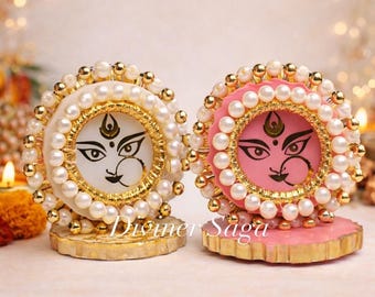 May include: Two decorative round pieces, one white and one pink, each featuring a painted face with intricate details. The faces are surrounded by a ring of pearls and gold accents. The bases are gold and beige.