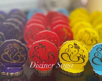 May include: Colorful, decorative figurines of the Hindu deity Ganesha. The figurines are in various colors, including purple, red, yellow, and blue, with a gold-colored outline and black script. The text "Diviner Saga" is visible.
