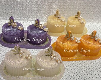 May include: Decorative resin trinket boxes in purple, yellow, orange, and white. Each box has a lid, sits on a matching tray, and is adorned with gold-colored leaves and faux pearls. The text "Diviner Saga" is visible on each tray.