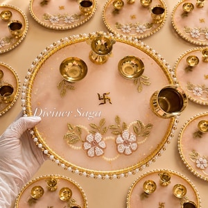 May include: A collection of decorative, round, pink and gold trays with floral and pearl accents. Each tray features small gold bowls and a central symbol. The text "Diviner Saga" is visible on one tray.