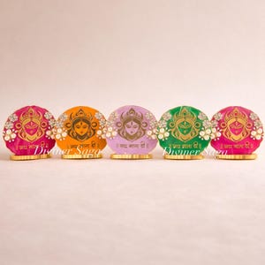 May include: A row of five colorful, round decorative pieces. Each piece features a deity image, floral accents, and the text "Diviner Saga" and other text in a foreign language. The pieces are in shades of pink, orange, purple, green, and pink.