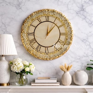 Puede incluir: Un reloj de pared redondo con una esfera de madera clara y números romanos dorados. El reloj tiene manecillas doradas y un borde texturizado de color dorado. El texto "Divine Saga" es visible en la esfera del reloj. El reloj está colgado en una pared de mármol.