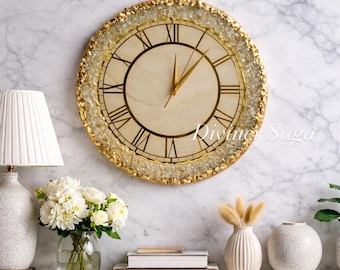 May include: A round wall clock with a light wood face and gold Roman numerals. The clock has gold hands and a gold-colored, textured border. The text "Divine Saga" is visible on the clock face. The clock is hanging on a marble wall.