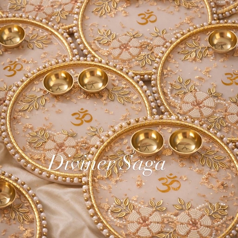 May include: Ornate, gold-colored decorative plates with floral and leaf designs, small brass bowls, and the Om symbol. The plates have a pearl-like border and the text "Diviner Saga".