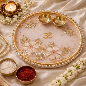 May include: A decorative, round, white and gold tray with floral and leaf accents. The tray features two small gold bowls, the Om symbol, and the text "Diviner Saga". Additional elements include a candle, flowers, and small bowls.