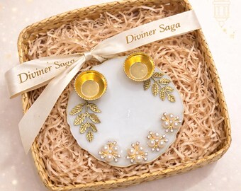 May include: A decorative white marble tray with two gold candle holders, gold leaf accents, and pearl and rhinestone embellishments. The tray sits in a woven basket with a ribbon that reads "Diviner Saga".