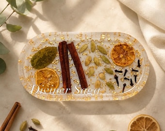 May include: Oval resin tray with gold leaf flakes, cinnamon sticks, dried orange slices, cardamom pods, cloves, and a green leaf. The tray has the text "Diviner Saga" in gold.