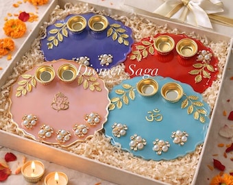 Puede incluir: Un juego de cuatro bandejas decorativas coloridas en una caja de regalo. Cada bandeja es de un color diferente: morado, rojo, rosa y azul. Cuentan con detalles de hojas doradas, adornos de perlas y pequeños candelabros dorados. La caja está llena de papel triturado.