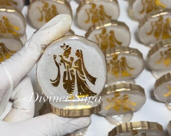 May include: White and gold resin coasters with a gold illustration of a couple. The coasters have a gold trim and are displayed in a group. The text "Diviner Saga" is visible on one of the coasters.