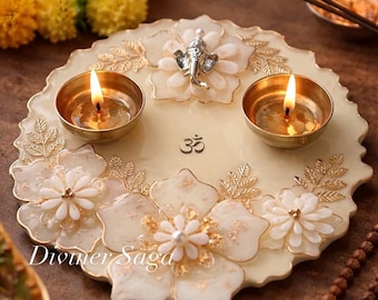 May include: A decorative cream-colored tray with floral and leaf designs, two lit brass candle holders, and a small silver statue. The tray has the text "Diviner Saga" and the Om symbol.