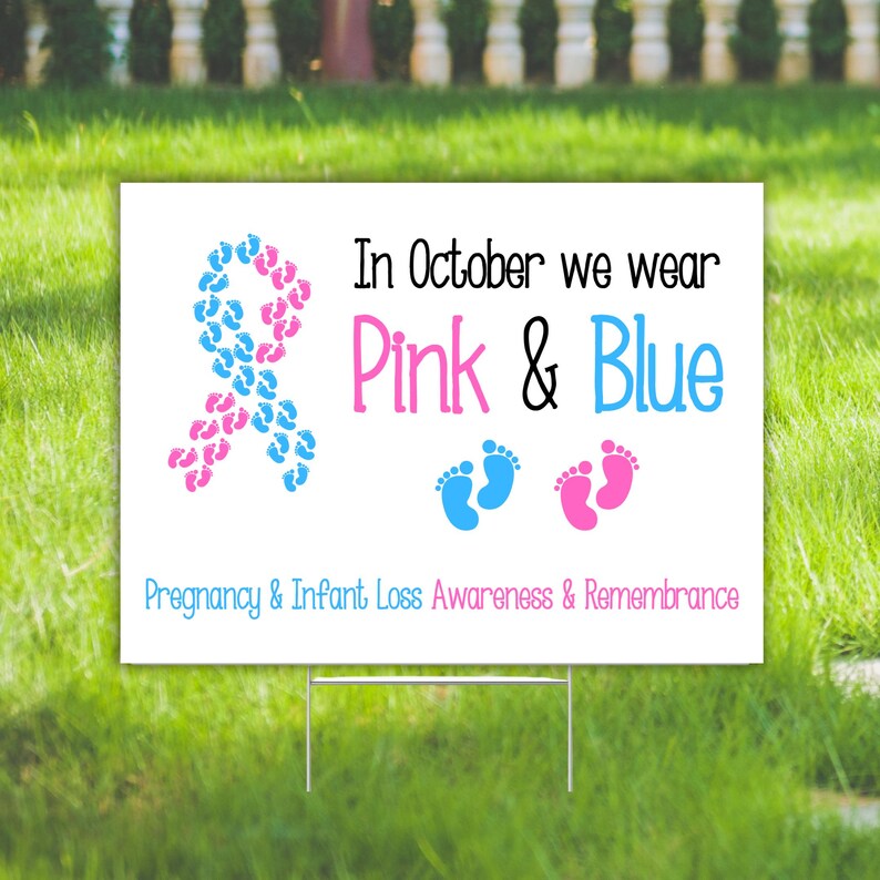 Pode incluir: Placa de jardim branca com o texto "In October we wear Pink & Blue" e "Pregnancy & Infant Loss Awareness & Remembrance". A placa tem uma fita feita de pegadas azuis e rosas.