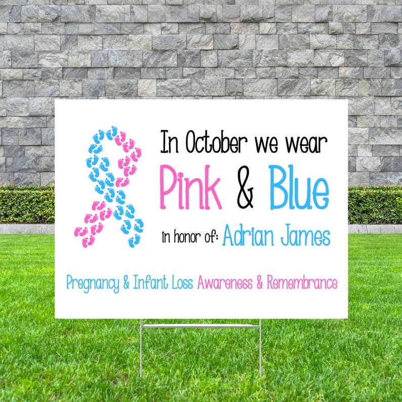 Pode incluir: Uma placa branca em um suporte de metal com texto e uma fita feita de pegadas rosa e azuis. A placa diz: "Em outubro vestimos rosa e azul em homenagem a: Adrian James. Conscientiza&ccedil;&atilde;o e lembran&ccedil;a da perda gestacional e infantil."