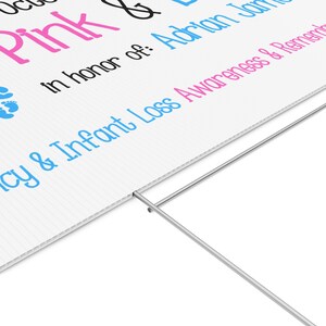 Pode incluir: Placa branca com texto rosa e azul, incluindo as palavras "Pink & Blue" e "Conscientiza&ccedil;&atilde;o e lembran&ccedil;a da perda infantil". A placa &eacute; suportada por uma estaca de metal.