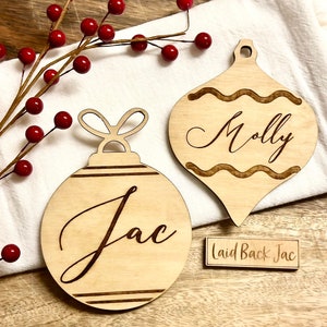 May include: Two wooden Christmas ornament place cards with the names "Molly" and "Jac" engraved on them. A smaller wooden sign reads "Laid Back Jac".