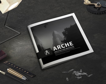 Puede incluir: Folleto en blanco y negro titulado "ARCHE ARCHITECTURE BROCHURE" con un edificio moderno en la portada. Sobre una superficie gris oscuro, con una lámpara de madera, bolígrafo, regla y clips.