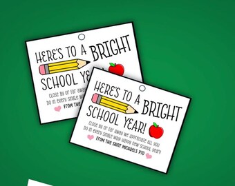 Op de afbeelding: Twee witte cadeaulabels met de tekst "HERE'S TO A BRIGHT SCHOOL YEAR!" met een gele potlood- en rode appelillustratie. De labels bevatten ook een bericht en een hartsymbool.