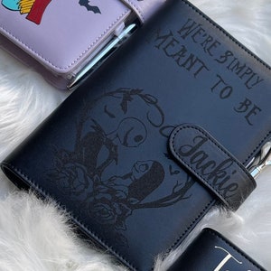 Puede incluir: Planificador de cuero negro con un diseño floral y el texto "We're simply meant to be" y "Jackie".