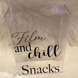 May include: Clear plastic container with a scalloped rim. The container has a black vinyl sticker with the text "Film and chill Snacks".