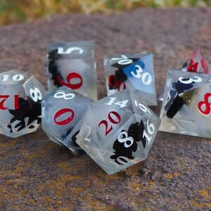 May include: Six clear dice with black and white designs and red numbers. The dice are on a brown, textured surface.