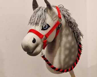 May include: A gray and white horse head with a red and black halter and lead rope. The horse head is made of fabric and is a toy.
