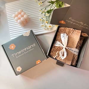May include: A green box with the text "Timeinhand handmade from nature" and a floral design. The box is open and inside is a brown paper with white tissue paper and the text "Just for you".