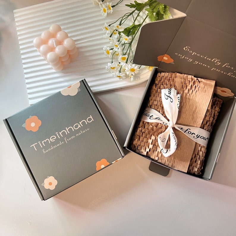 May include: A green box with the text "Timeinhand handmade from nature" and a floral design. The box is open and inside is a brown paper with white tissue paper and the text "Just for you".