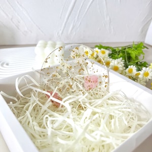 May include: A round, clear resin coaster with dried flowers and gold flakes. The coaster is in a white box with white shredded paper.