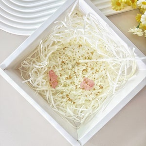 May include: A white square box with a white paper filler inside. The box contains a clear resin paperweight with pink and gold accents.