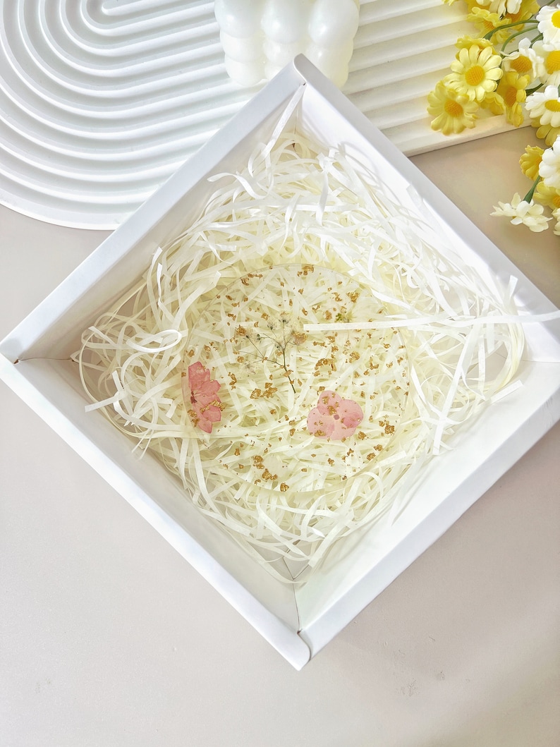 May include: A white square box with a white paper filler inside. The box contains a clear resin paperweight with pink and gold accents.
