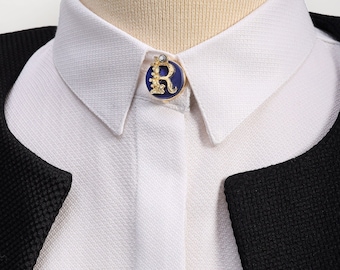 May include: A white collared shirt with a blue and gold pin featuring the letter "R" on the collar.