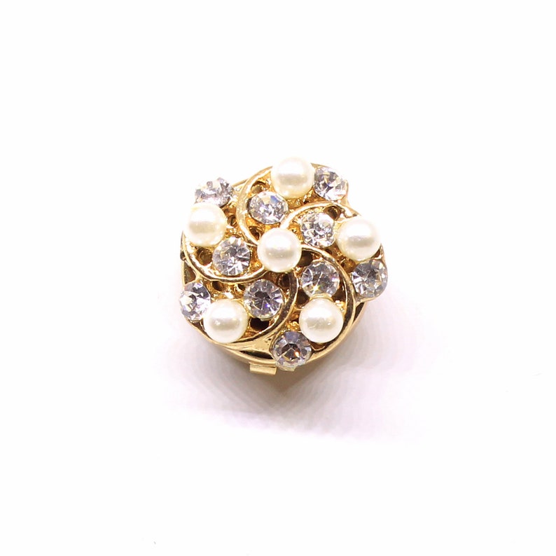 Peut inclure: Une broche dor&eacute;e avec un motif en spirale orn&eacute; de perles blanches et de strass transparents.