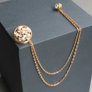 Peut inclure: Une cha&icirc;ne en or avec une broche ronde en perles et strass. La cha&icirc;ne est &agrave; double brin et comporte un petit strass rond en haut.