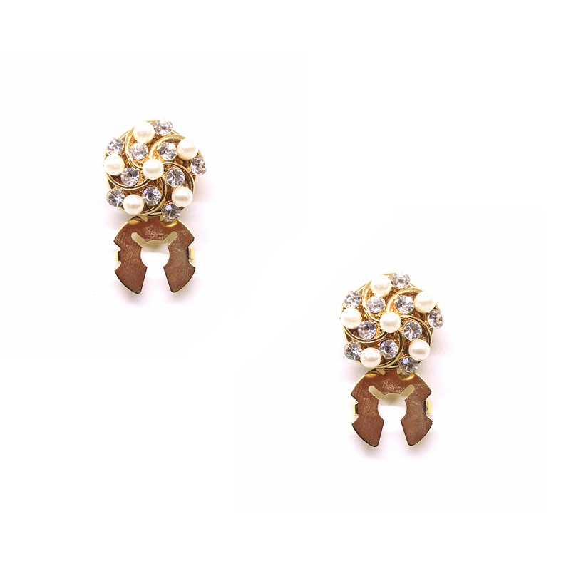 Peut inclure: Une paire de boucles d'oreilles dor&eacute;es avec un motif en spirale orn&eacute; de perles blanches et de strass transparents. Les boucles d'oreilles ont une fermeture &agrave; clip.
