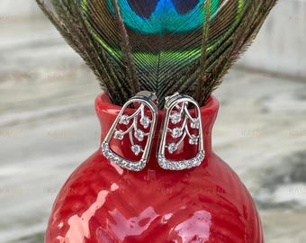 May include: A pair of silver earrings with a delicate floral design and clear cubic zirconia stones. The earrings are displayed on a red ceramic vase.