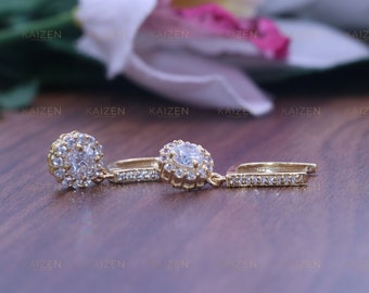 May include: A pair of gold earrings with a round, clear stone surrounded by smaller stones. The earrings have a simple, elegant design.