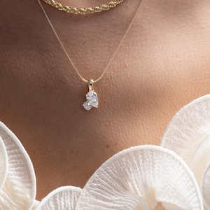 May include: Three gold necklaces with diamond pendants. The top necklace is a delicate chain, the middle one is a rope chain, and the bottom one has a cluster pendant. The necklaces are layered and worn on a person.