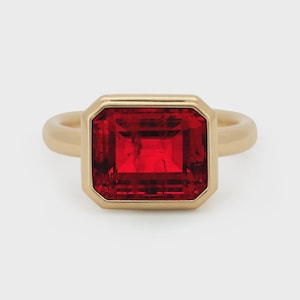 Puede incluir: Una taza de cerámica blanca con un asa negra y el texto "But First, Coffee" en un estilo manuscrito. La taza está sobre una superficie blanca. La taza mide aproximadamente 10 cm de alto.