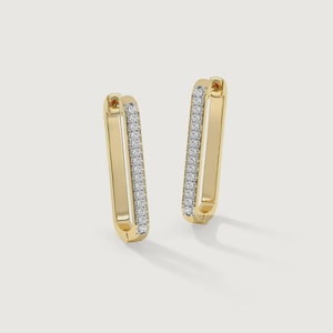 Könnte beinhalten: Ein Paar goldfarbene, rechteckige Creolen. Jeder Ohrring hat eine Reihe kleiner, klarer Edelsteine entlang der Innenkante. Die Ohrringe werden vor einem hellen Hintergrund gezeigt, der ihr Design und ihren Glanz hervorhebt.