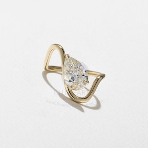 May include: A gold ring with a pear-cut diamond. The ring's design is distinctive, with a flowing, curved band that cradles the diamond. The diamond's facets create a brilliant sparkle.